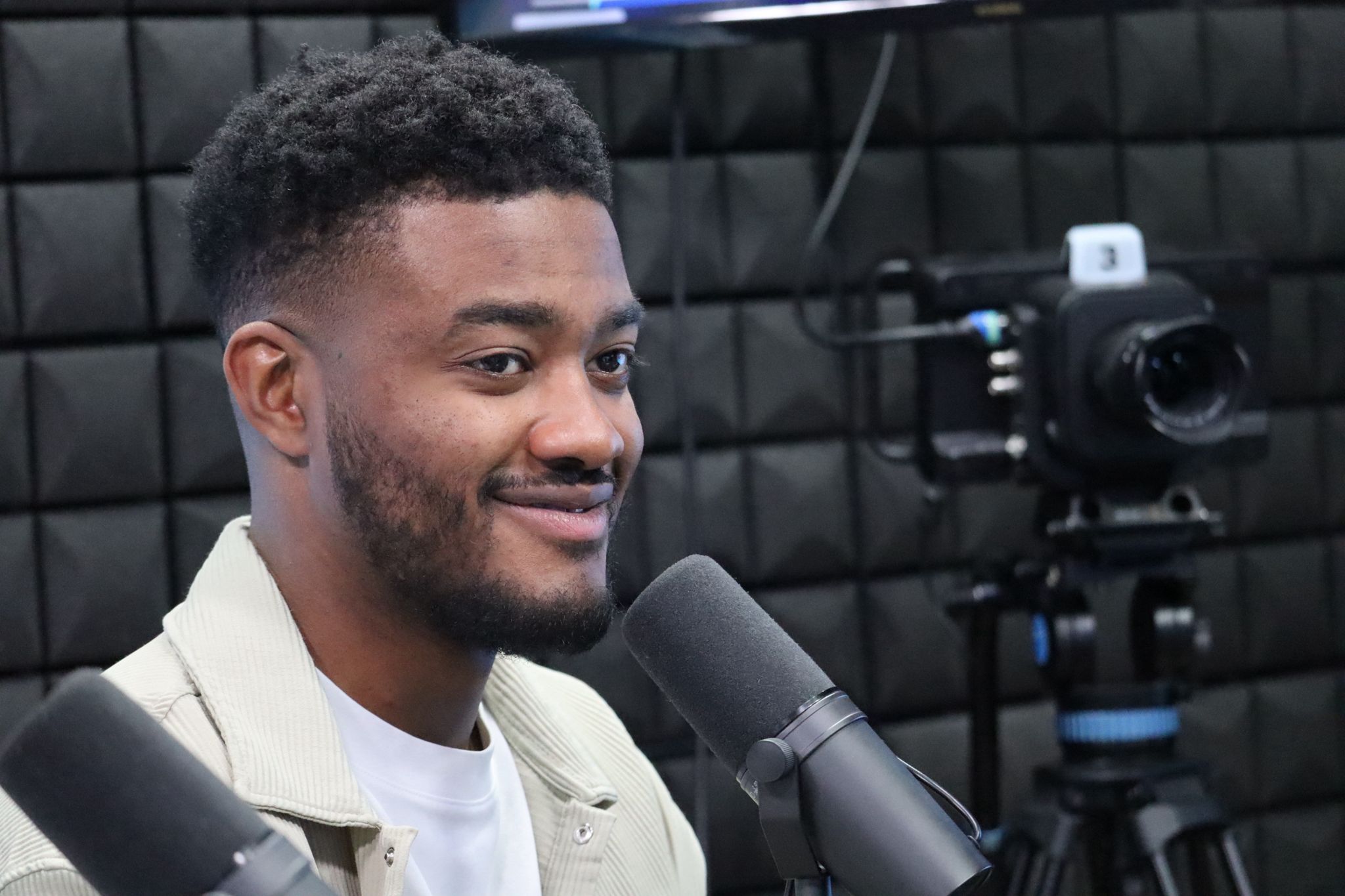 Interviewé souriant en studio d'enregistrement face au micro, caméra en arrière-plan